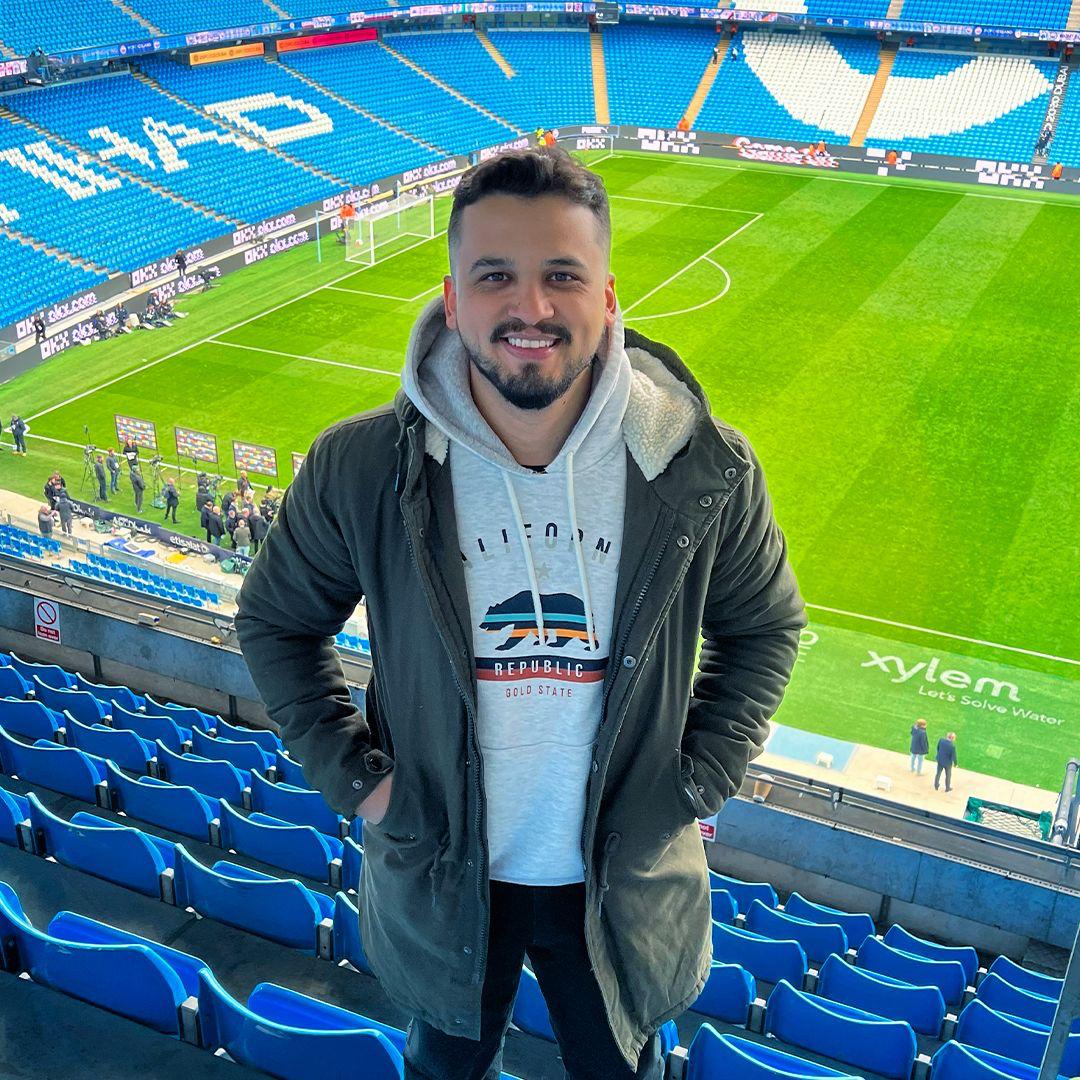 Thiago em pé na arquibancada de um estádio na Europa
